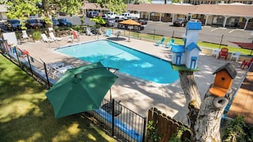Una piscina con sillas de descanso y sombrillas, rodeada por una valla y árboles.