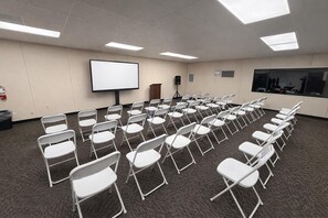 A conference room with rows of white folding chairs, a large projection screen, a podium, and a carpeted floor. - Skylark Shores Resort (Lakeport)