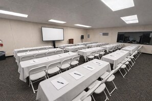 A conference room with white tables and chairs, a projector screen, and a large window. - Skylark Shores Resort (Lakeport)