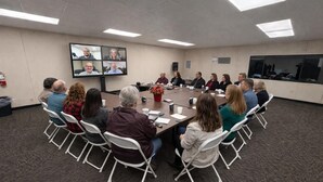 A conference room with a large table, chairs, a screen displaying multiple video feeds, and a potted plant. - Skylark Shores Resort (Lakeport)