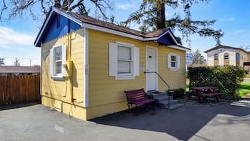 Un edificio amarillo con techo azul, cerca de madera, un banco y una mesa de picnic.