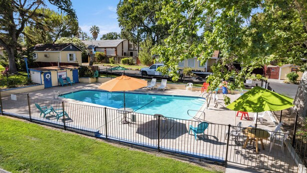 A rectangular swimming pool with a fenced deck, surrounded by trees and a small building. - Skylark Shores Resort (Lakeport)