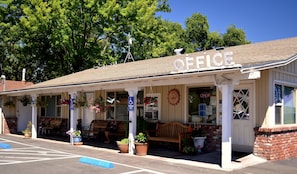 A small, single-story building with a covered porch, a sign that reads "OFFICE", and several potted plants.
