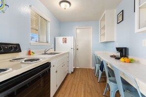 A kitchen with a stove, sink, refrigerator, and a dining area with chairs and a table.
