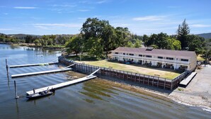A lakeside hotel with a dock, a boat, and a building with a lawn and outdoor seating. - Skylark Shores Resort (Lakeport)