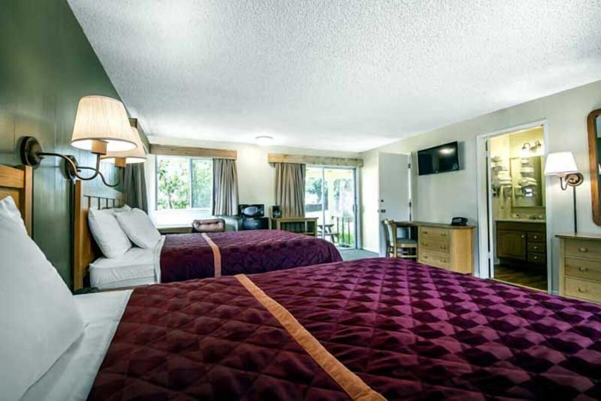 A hotel room with two beds, a desk, a chair, a TV, and a bathroom.