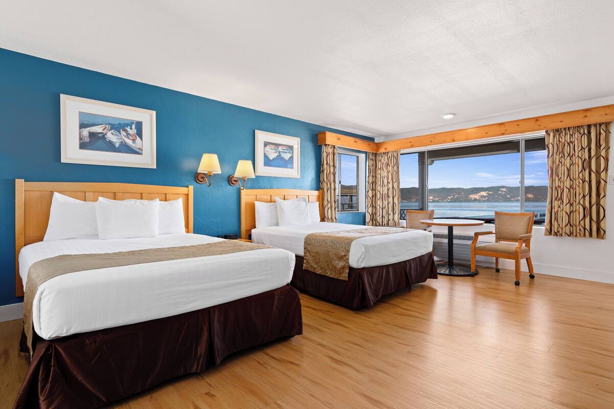 Habitación de hotel con dos camas, una mesa de comedor y vista al mar.