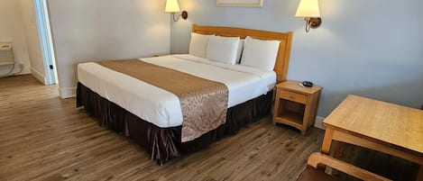 Una habitación de hotel con una cama grande, dos lámparas de noche, una mesita de noche de madera, una pequeña mesa y una puerta que da a otra habitación.