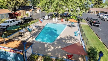 A rectangular pool with a surrounding deck, lounge chairs, and a covered seating area.