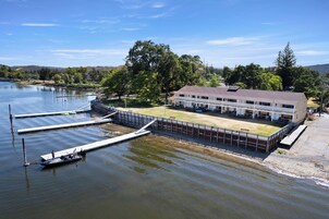 A lakeside hotel with a dock, a boat, and a building with a lawn and outdoor seating.