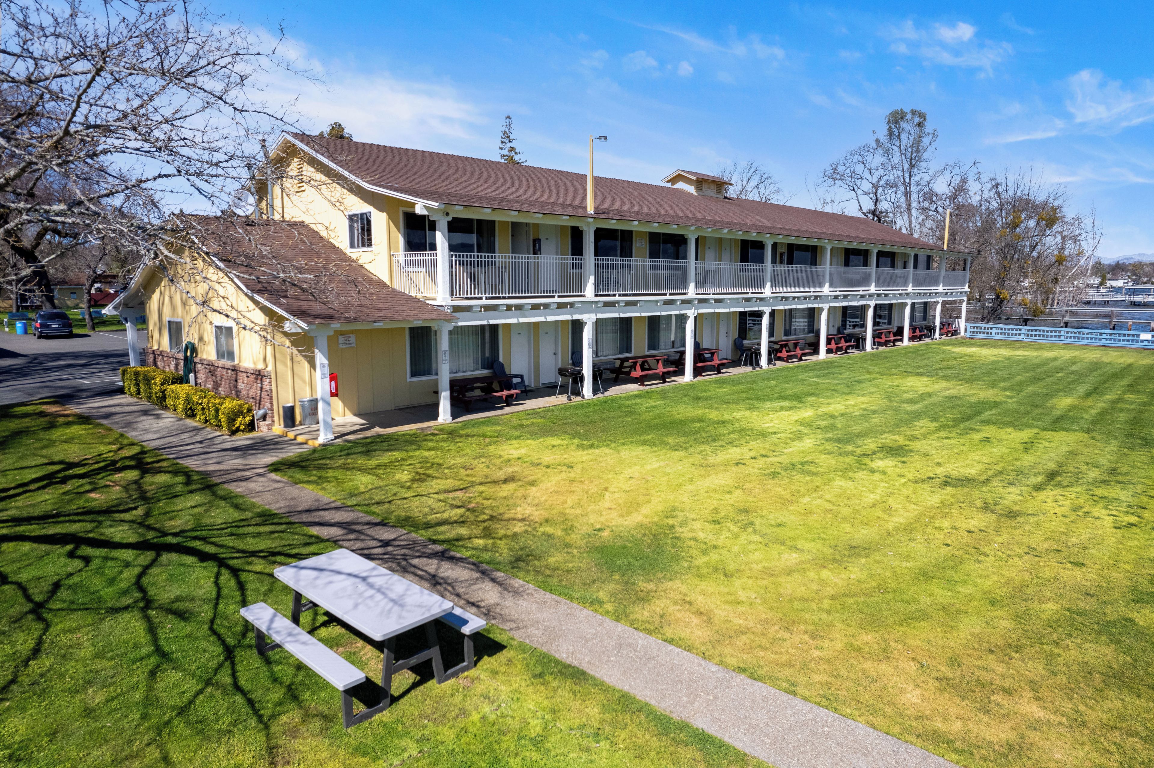 A two-story motel with a covered patio area, outdoor seating, and a well-maintained lawn.