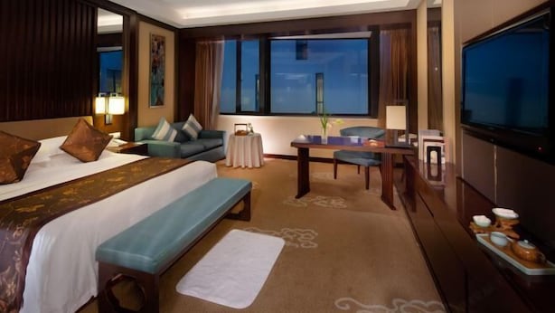 A hotel room with a large bed, a desk, a chair, a TV, and a view of the night sky. - Xianheng Hotel (Shaoxing)
