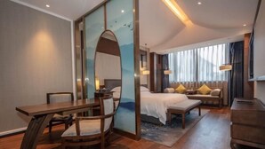 A modern hotel room with a wooden dining table, a large bed with a white comforter, a sofa with cushions, and a large mirror. - Xianheng Hotel (Shaoxing)