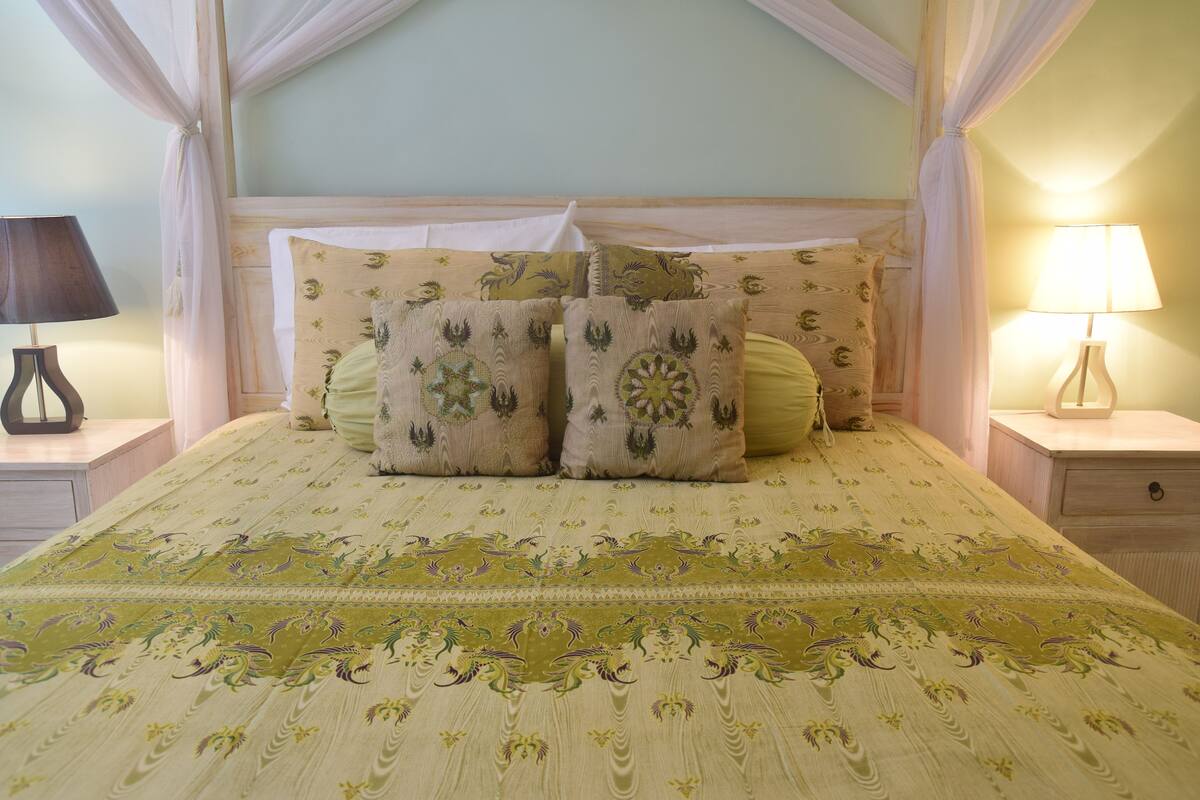 Una cama con dosela, dos mesitas de noche con lámparas y una colcha estampada.