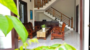 A spacious living area with a staircase, wooden furniture, and a potted plant. - Yen Villa Hoi An (Da Nang)