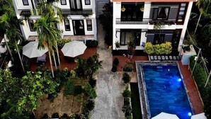 A residential building with a swimming pool, surrounded by palm trees and greenery. - Yen Villa Hoi An (Da Nang)
