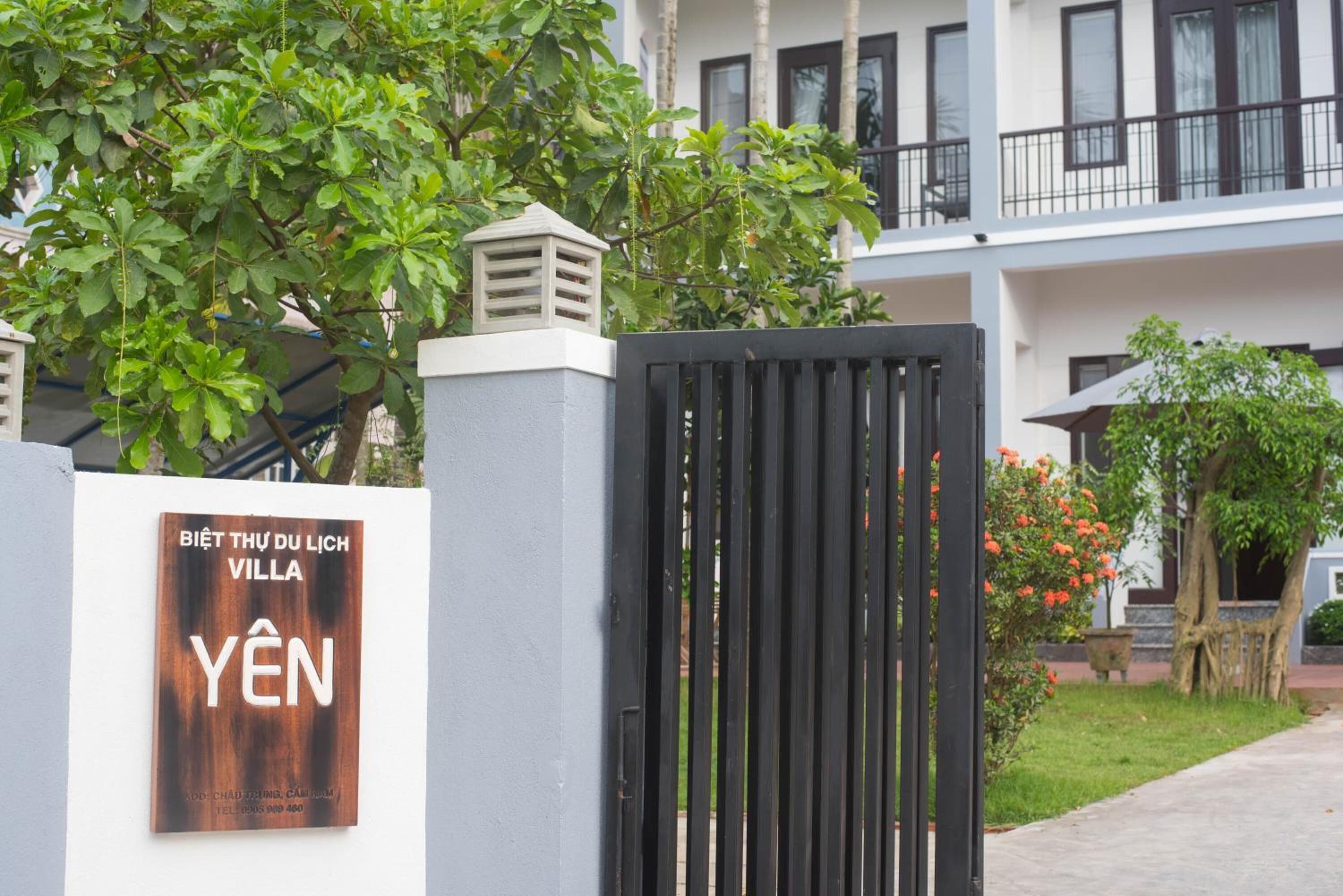 A villa with a gated entrance, a signboard, and a building in the background.