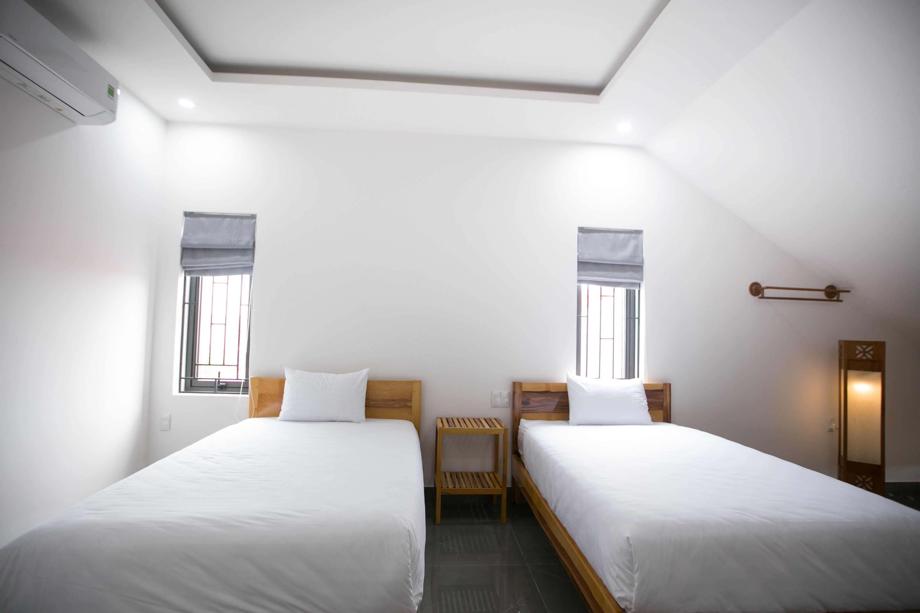 A clean, modern hotel room with two single beds, a small wooden nightstand, a mirror, and a window with a view.