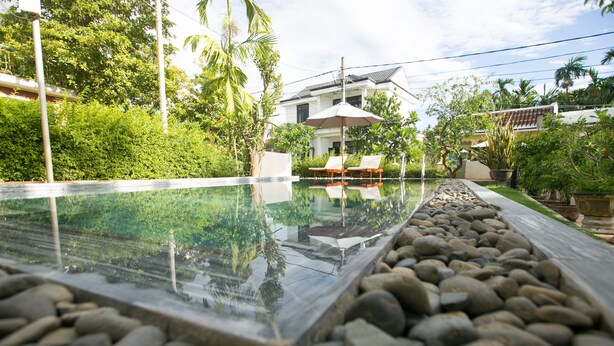 A swimming pool with a clear glass edge, surrounded by a stone border. There are lounge chairs and an umbrella near the pool. - Yen Villa Hoi An (Da Nang)