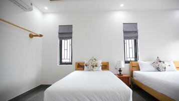Habitación de hotel con dos camas, cabecero de madera, mesita de noche con lámpara y ventana con persiana.