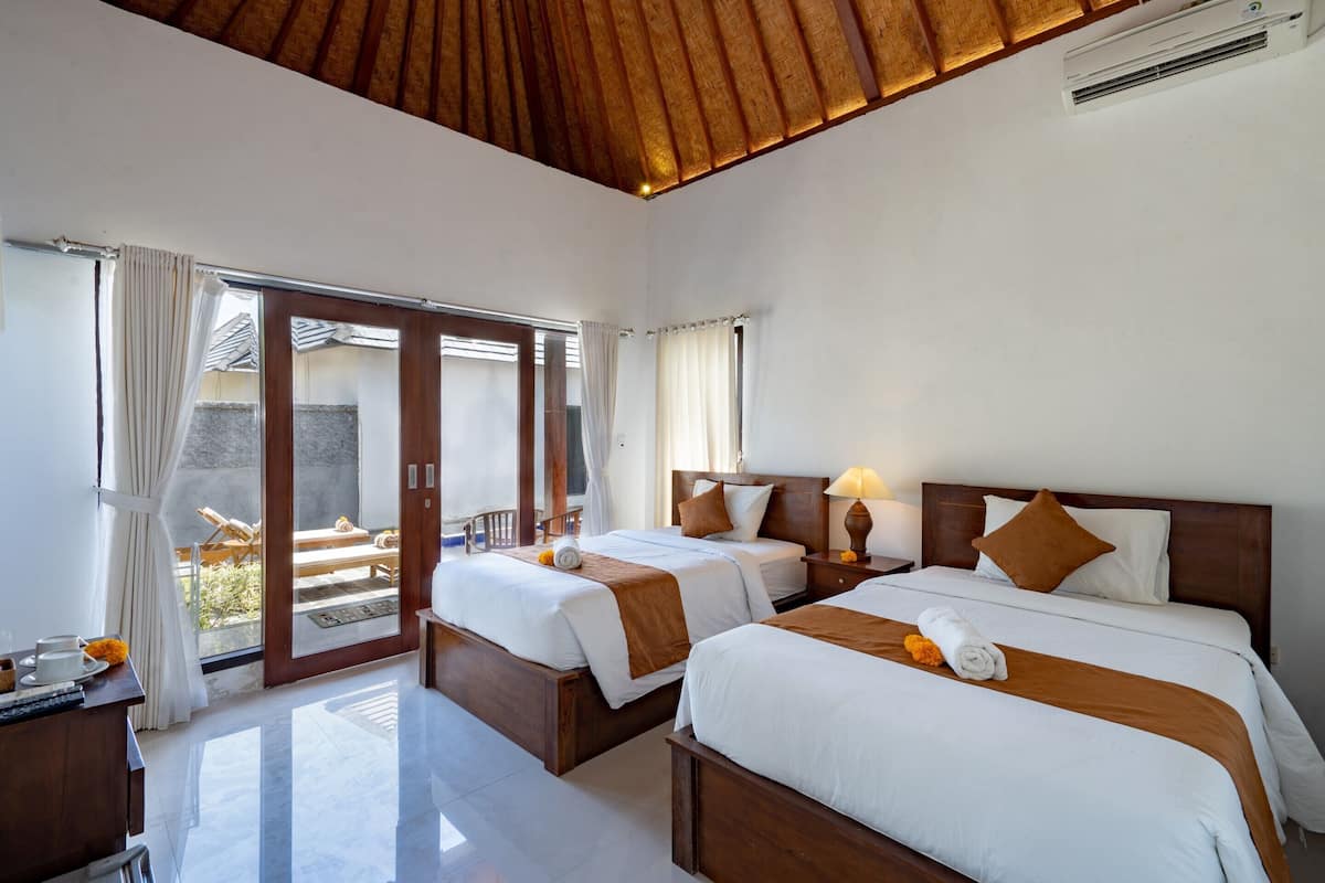 Habitación de hotel con dos camas, techo de madera y puerta corrediza de vidrio que da a un espacio exterior.