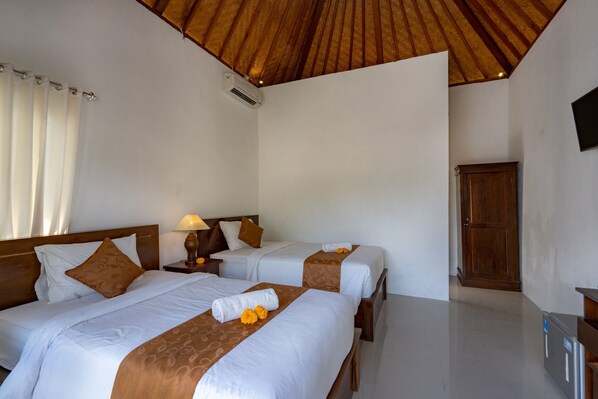 Habitación de hotel con dos camas, cabeceros de madera, ventilador de techo, armario de madera y televisor de pantalla plana.