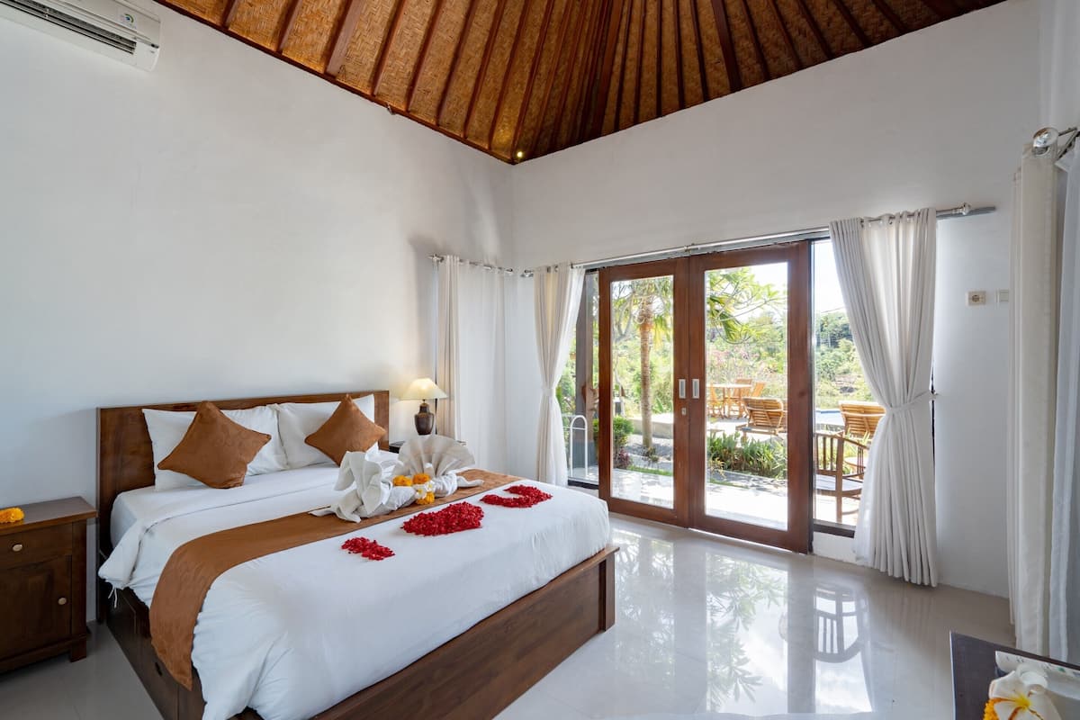 Un dormitorio amplio con una cama grande, cabecero de madera y vistas a un patio exterior con sillas y una mesa.