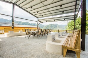 An outdoor seating area with a wooden bench and chairs, a concrete sink, and a view of mountains. - Baishengcun Coffee Farm (Guoxing)