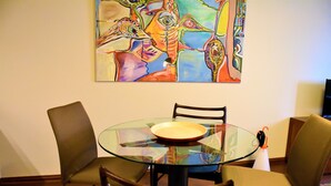 A dining area with a glass table, two chairs, and a colorful abstract painting on the wall. - Ribeira Oporto Apartment (New) (Porto)