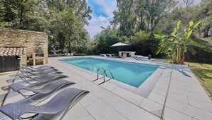 A rectangular swimming pool with a stone wall on one side, surrounded by lounge chairs and a covered seating area. - Private Island Medieval Watermill with Pool & River Access (Roquebrune)