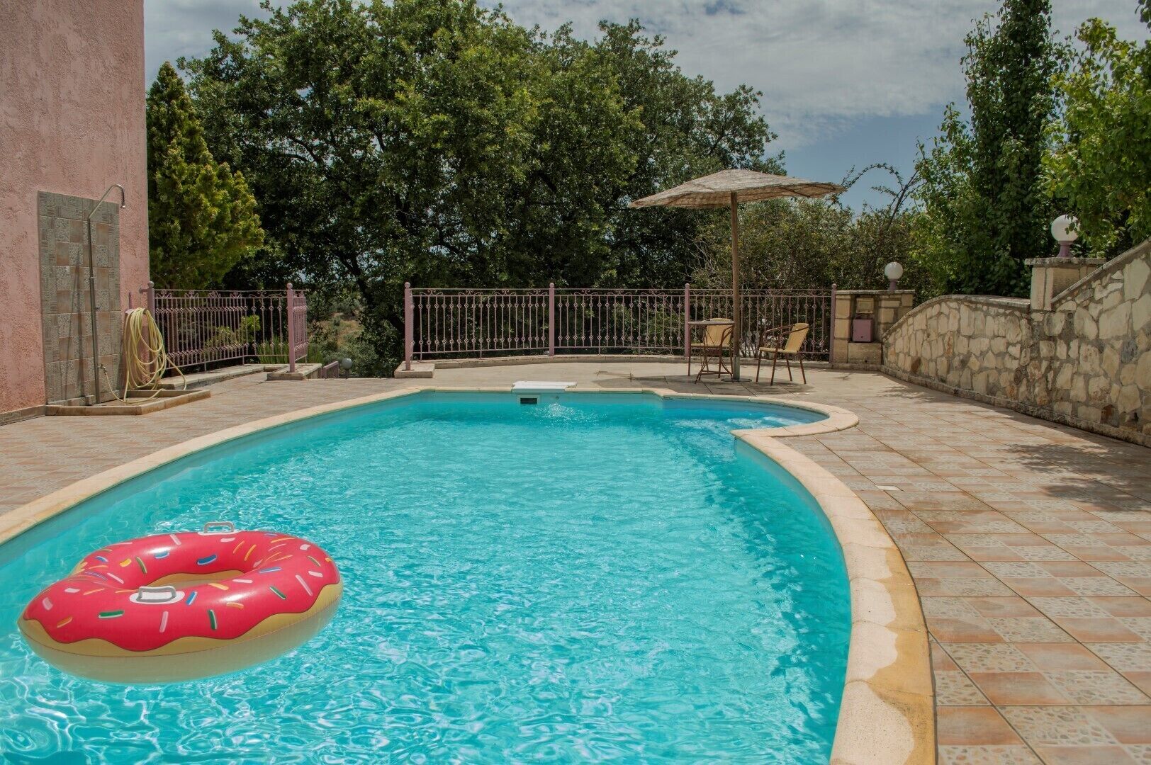 A swimming pool with a red donut-shaped float, surrounded by a stone wall and a metal fence.