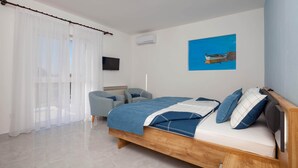 A bedroom with a wooden bed, a blue and white bedspread, a blue chair, a TV on the wall, and a painting of a boat.