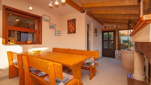 A wooden dining table with benches, a kitchen area with a stone counter, and a view of the outdoors through a door.