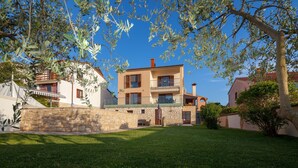 A two-story building with a stone wall and a grassy yard.