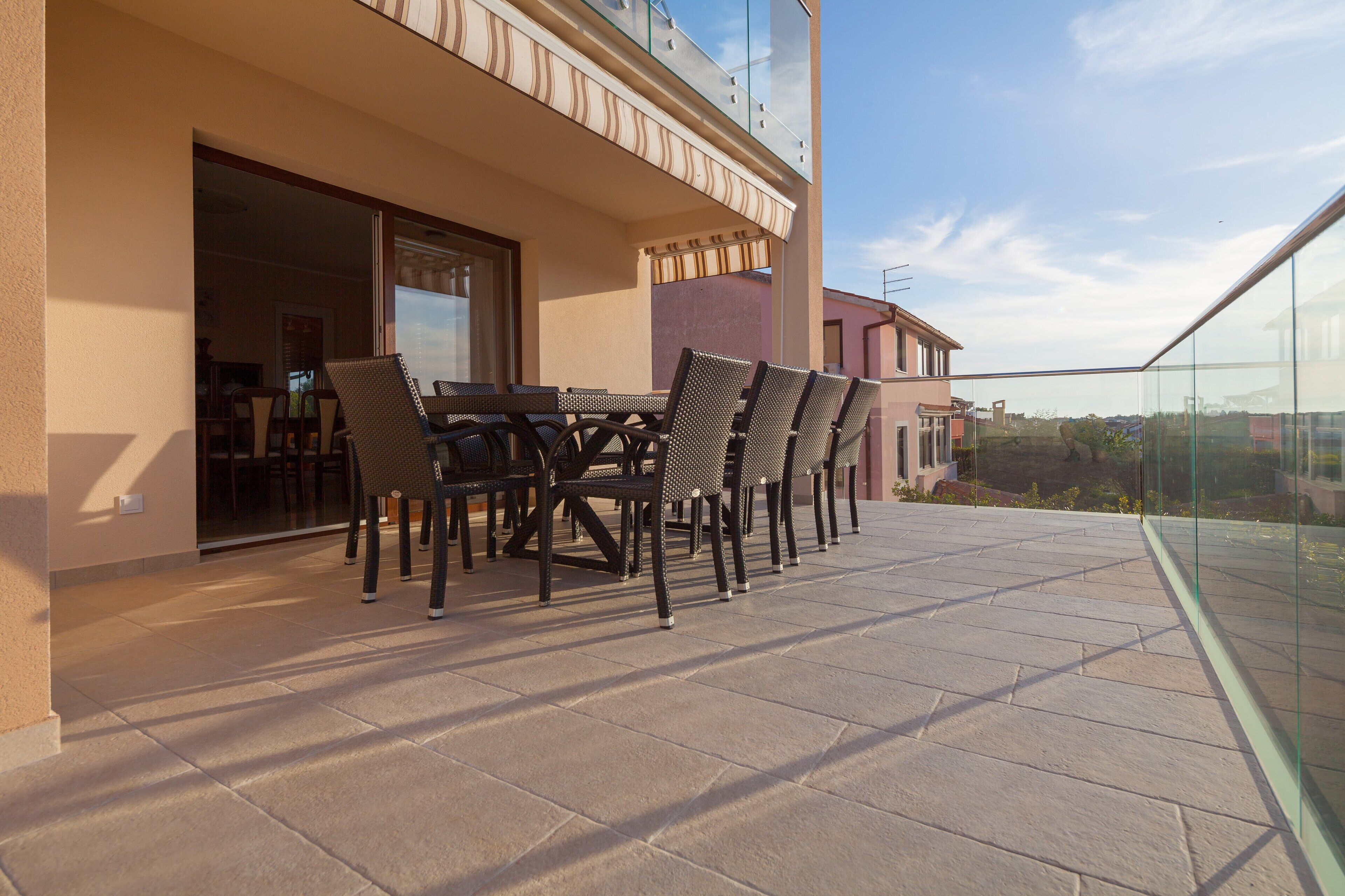 Un balcón con una mesa y sillas, barandilla de cristal y vistas de los edificios circundantes.