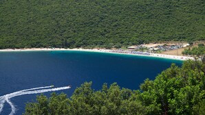 Une plage côtière aux eaux turquoise et limpides, bordée d’un rivage sablonneux, avec une forêt verdoyante et luxuriante en arrière-plan.