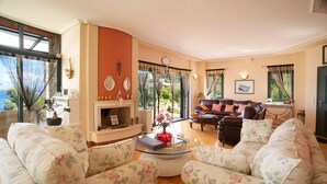 Un salon avec des canapés à motifs floraux, une cheminée et de grandes fenêtres avec des rideaux.