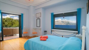 Une chambre avec un lit, une chaise, une fenêtre donnant sur la mer et un balcon avec une table et des chaises.