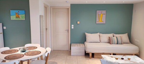 A small, cozy room with a sofa, a dining table with chairs, and two paintings on the walls. - The Garden of Zephyrus – West | Nature & Amazing View (Pithari)