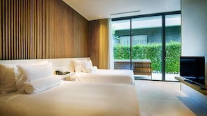 Una moderna camera d'hotel con due letti grandi, una televisione a schermo piatto e una porta vetrata scorrevole che dà su un balcone con piante.