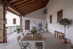 A covered patio area with a wooden table and chairs, potted plants, and a fire extinguisher.