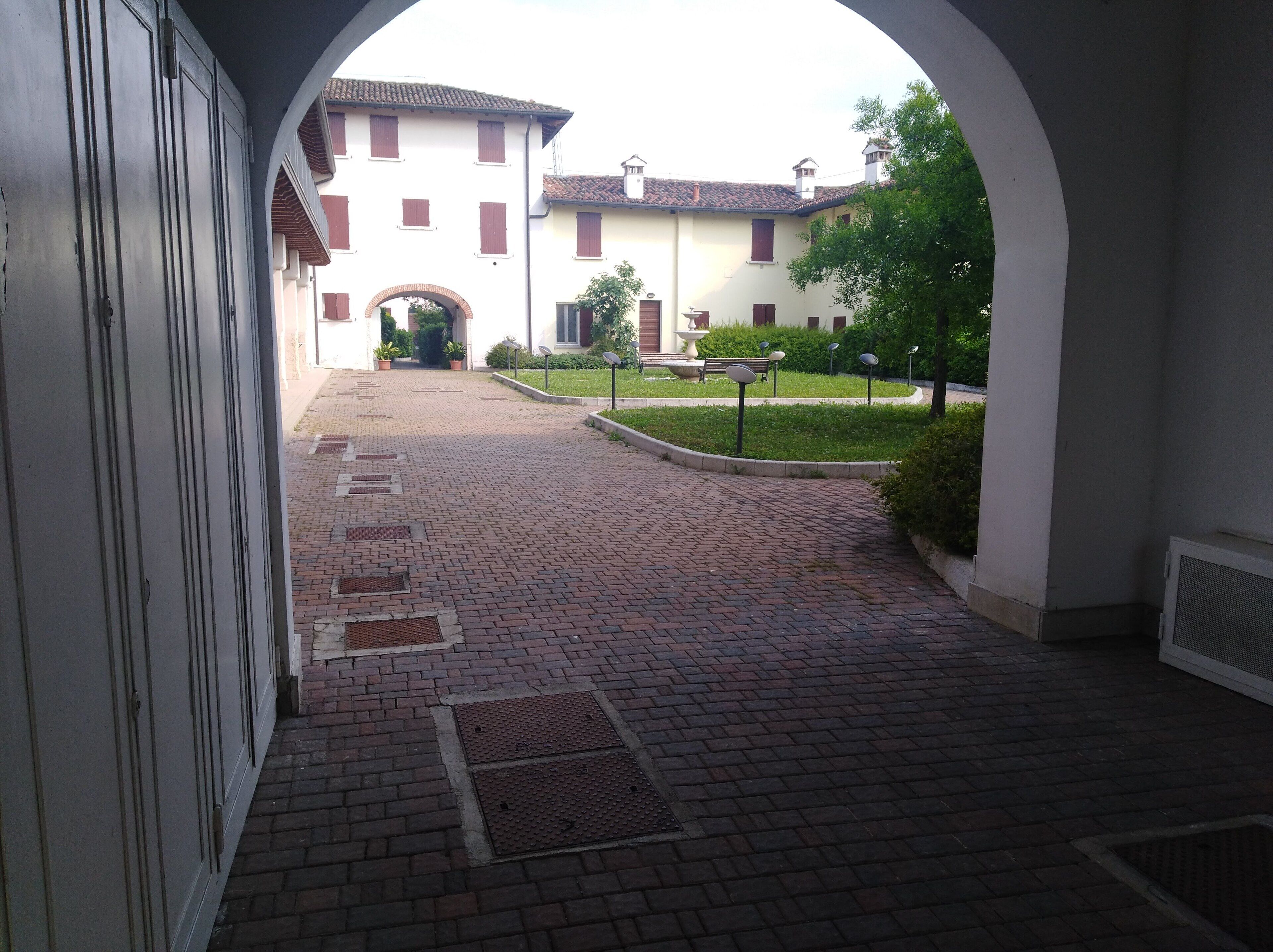 A courtyard with a brick pathway leading to a building with red shutters and a white facade.