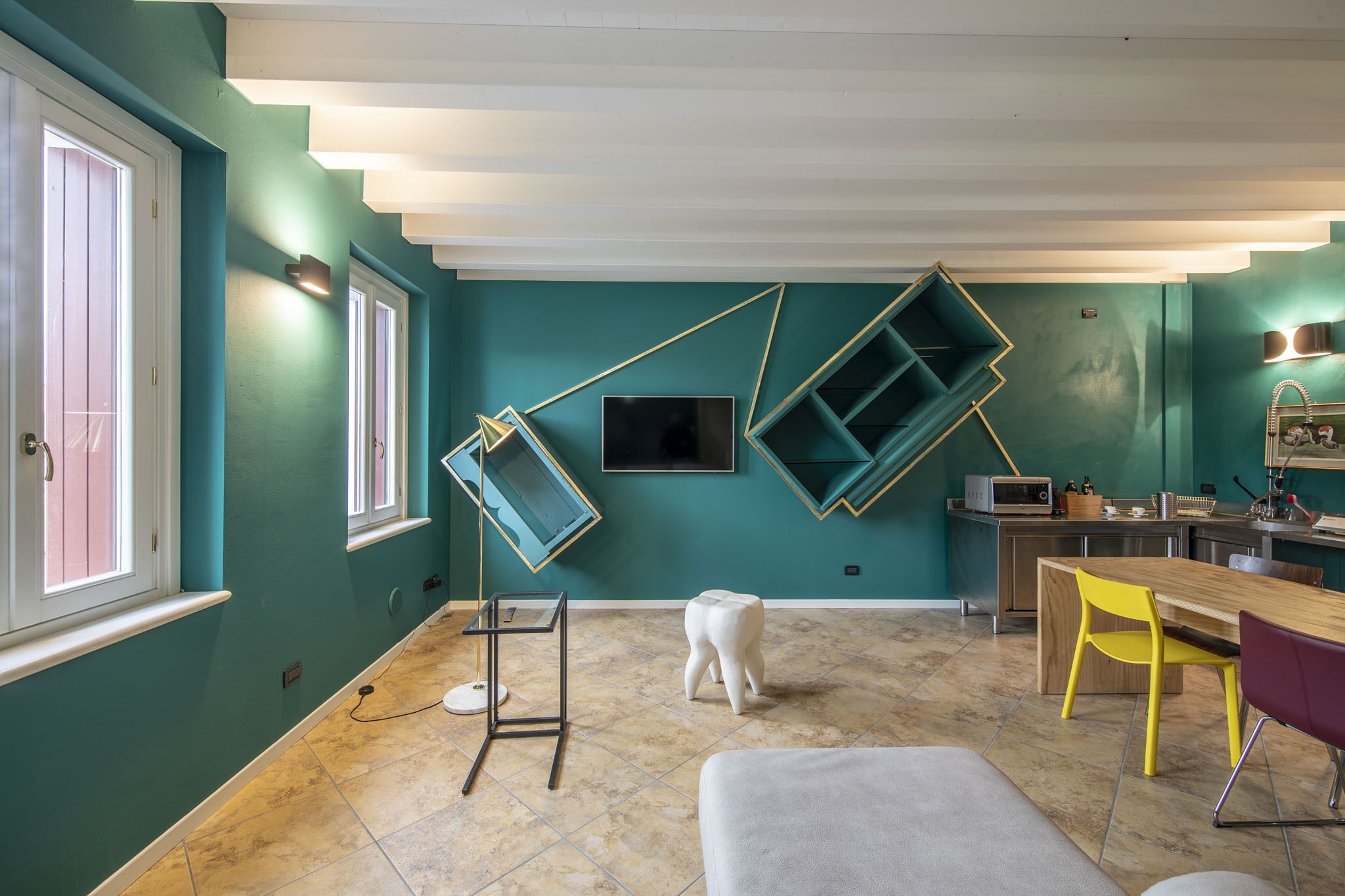 A modern kitchen with teal walls, a wooden dining table, and a built-in microwave.