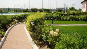 A paved pathway with a brick surface, bordered by lush green hedges and flowering plants. - "DESIGNcontrodesign  (desenzano)