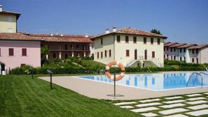 A swimming pool area with a lifebuoy, surrounded by well-maintained grass and a building with a tiled roof. - "DESIGNcontrodesign  (desenzano)