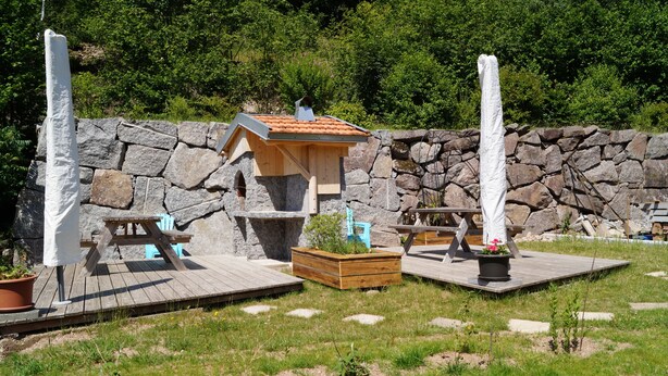 Un jardín con muro de piedra, bancos de madera y un comedero para pájaros.