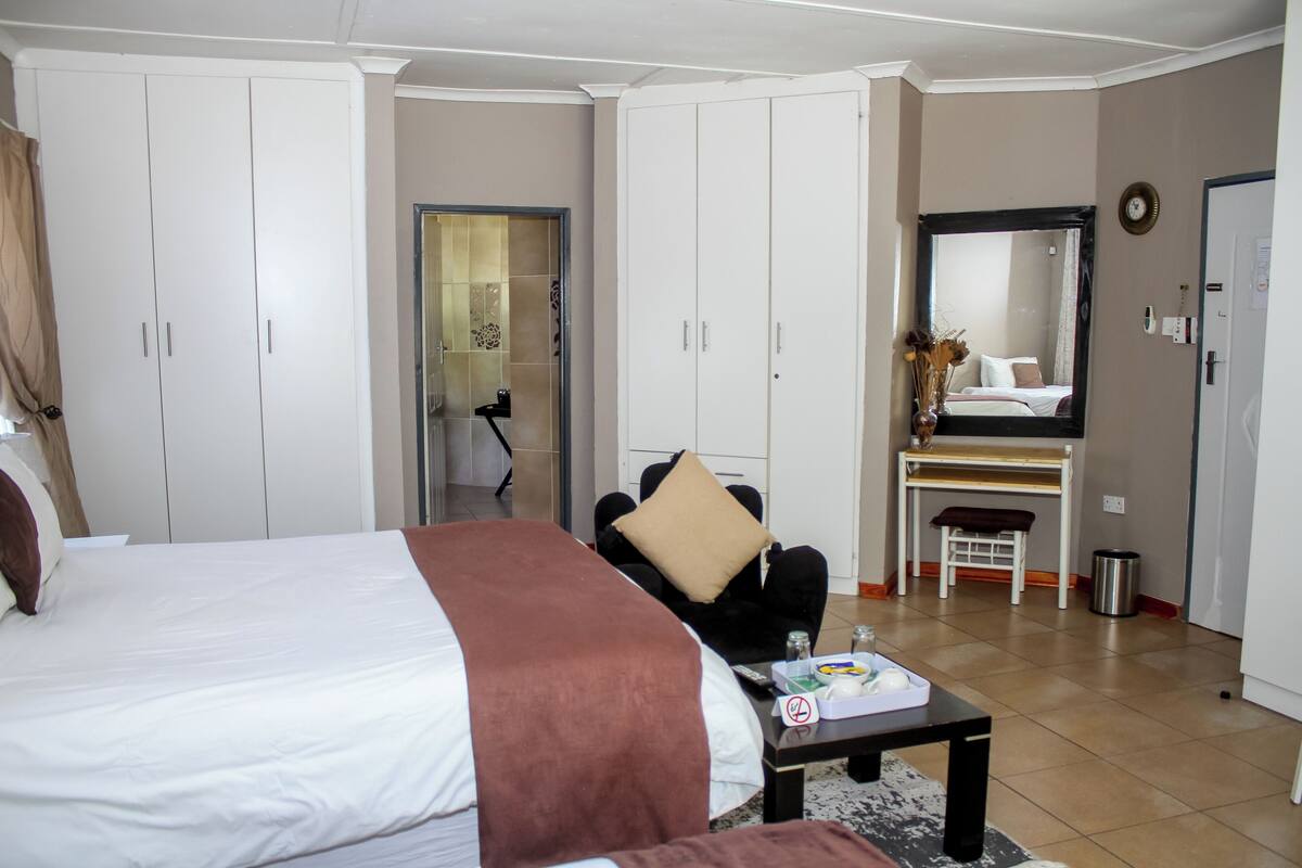A hotel room with a large bed, a desk, a chair, a mirror, and a wardrobe.