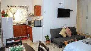 Un espacio habitable compacto con kitchenette, sofá, televisor y zona de comedor.