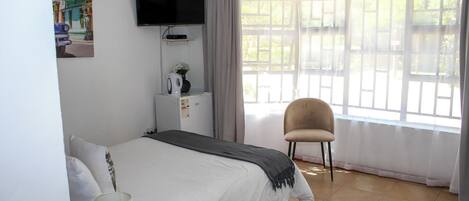 A bedroom with a bed, a TV mounted on the wall, a chair, and a window with curtains.