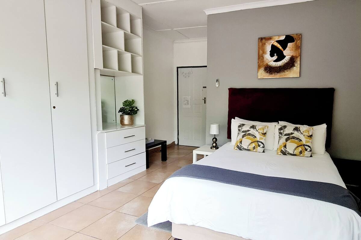 A bedroom with a bed, a wardrobe, a bedside table, and a wall with artwork.